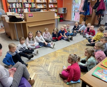 'Biedronki' siedzą na poduszkach oraz słuchają bajki, którą opowiada im Pani Bibliotekarka. - powiększ