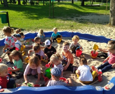 'Pszczółki' na zdjęciu grupowym podczas pierwszego wyjścia do ogrodu przedszkolnego. Dzieci bawią się w piaskownicy łopatkami i wiaderkami. - powiększ