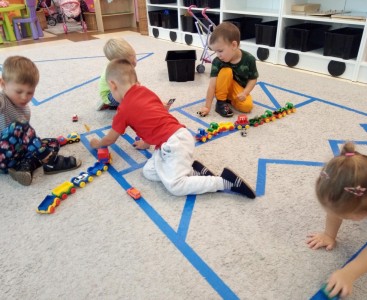 Na zdjęciu grupa dzieci, które uczą się figur geometrycznych, poruszania się w ruchu pieszym i drogowym, a przede wszystkim dobrze się bawią.  - powiększ