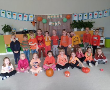 Dzieci z grupy 'Liski' na zdjęciu grupowym, ubrane na pomarańczowo, Chłopcy stoją z tyłu, a dziewczynki siedzą z przodu. Przed dziećmi leżą małe i duże dynie. - powiększ