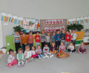 Dzieci z grupy 'Liski' na zdjęciu grupowym, na tle napisu 'Dzień Jabłka' oraz swoich prac plastycznych pt. 'Czerwone jabłuszka'. - powiększ