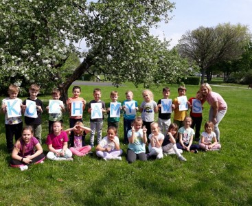 Grupowe zdjęcie gr. MYSZEK, które w rączkach trzymają napis  KOCHAMY WAS! Zdjęcie jest  niespodzianką z okazji Dnia Mamy i Taty. - powiększ