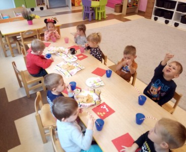 Zdjęcie przedstawia dzieci, które chętnie usiadły do stolików, żeby poczęstować się słodkościami. - powiększ